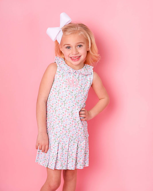 Young girl wearing a floral dress with a large white bow on a pink background