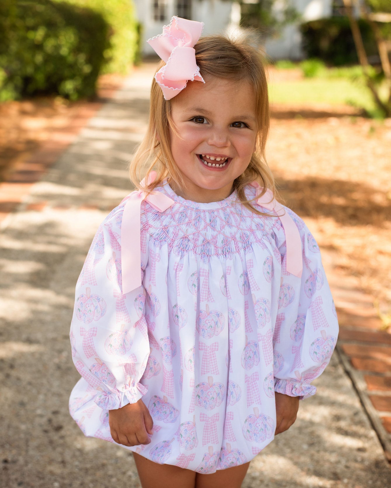 Young girl wearing a floral dress with pink suspenders outdoors.