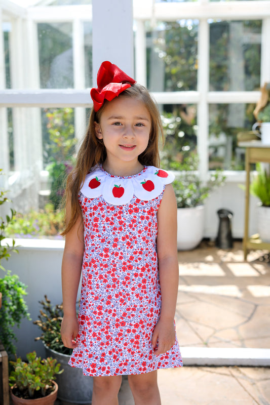 Young girl wearing a floral dress with scalloped collar wearing apples.