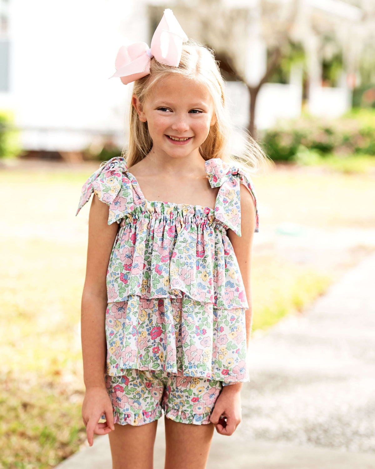 Young girl wearing a floral outfit with a pink bow in a park setting