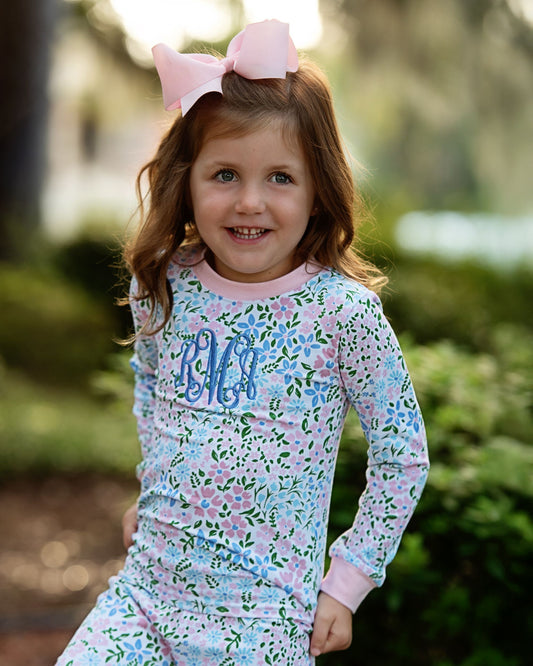 Young girl wearing a floral outfit with a pink bow, standing outdoors.