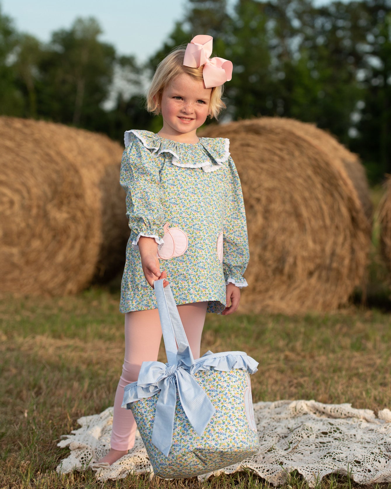 Young girl wearing a floral pumpkin legging set with a pink bow in her hair, standing outdoors 2