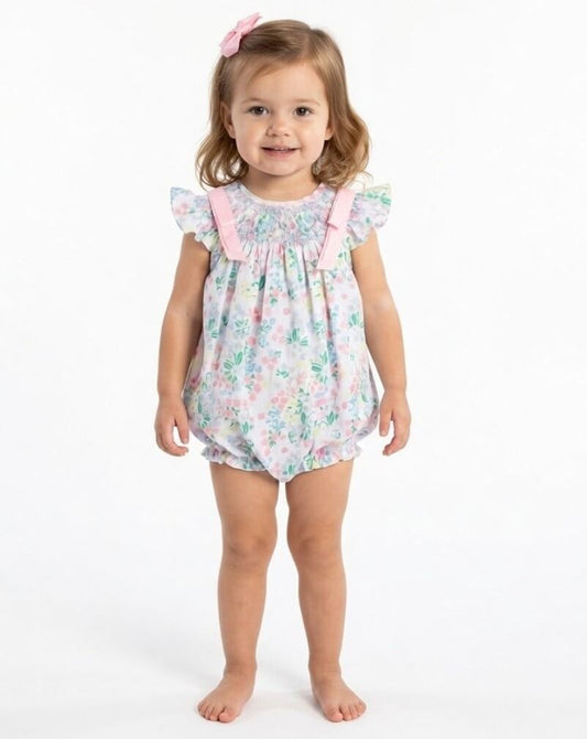 Young girl wearing a floral romper with pink straps on a white background
