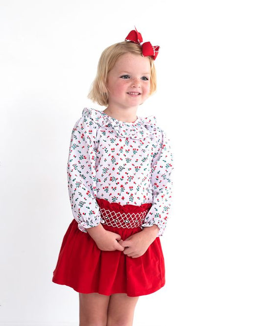 Young girl wearing a floral top and red skirt with a white background