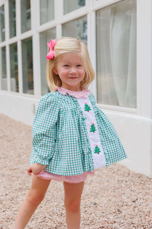 Young girl wearing a green checkered diaper set with embroidered Christmas tree patterns outdoors.