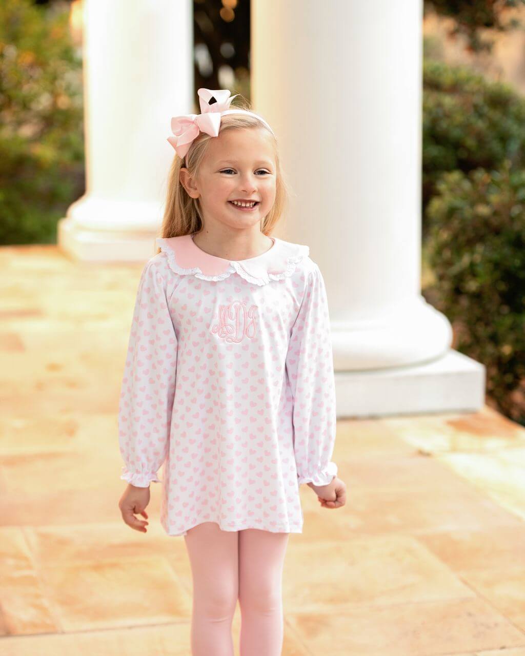 Young girl wearing a legging set with pink polka dots and a pink bow, standing outdoors.