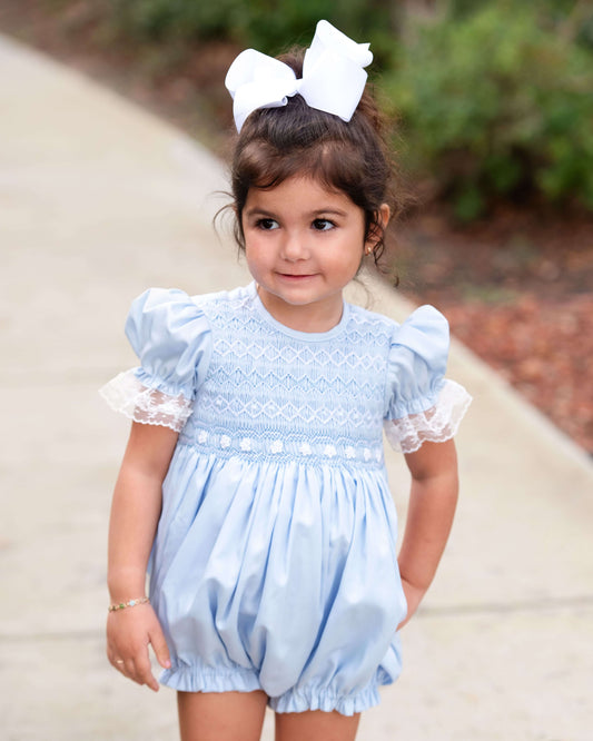 Young girl wearing a light blue dress with white lace details outdoors.