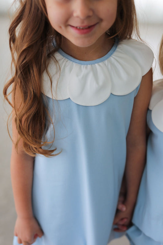 Young girl wearing a light blue dress with a white collar against a neutral background