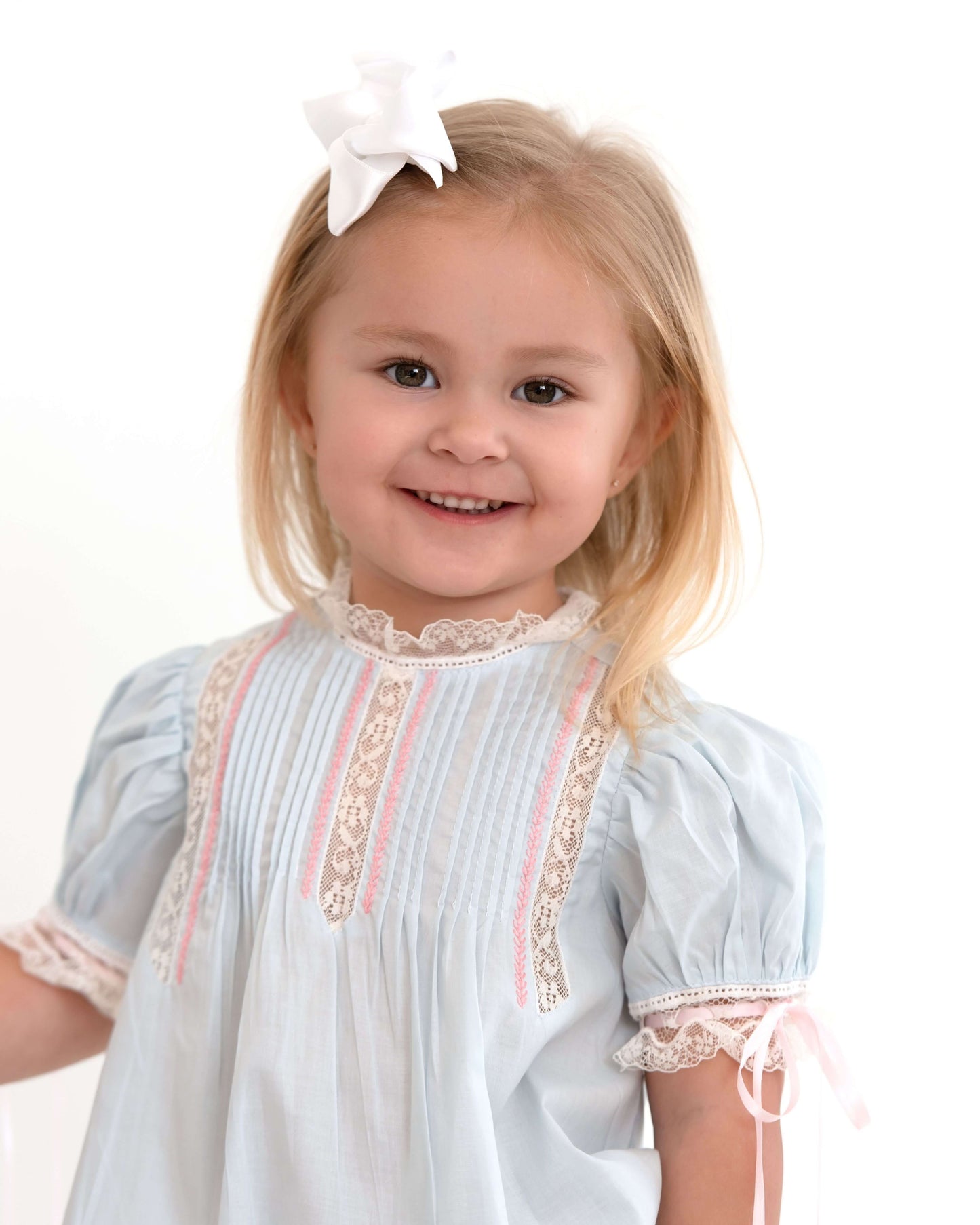 Young girl wearing a light blue dress with lace details on a white background