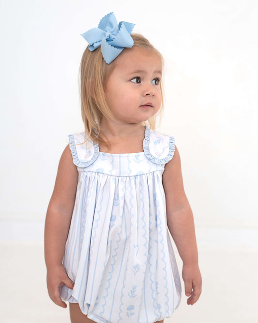 Young girl wearing a light blue dress with ruffles and a matching headband on a white background