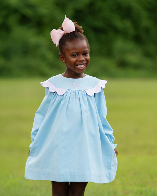 Young girl wearing a light blue dress with white collar in an outdoor setting