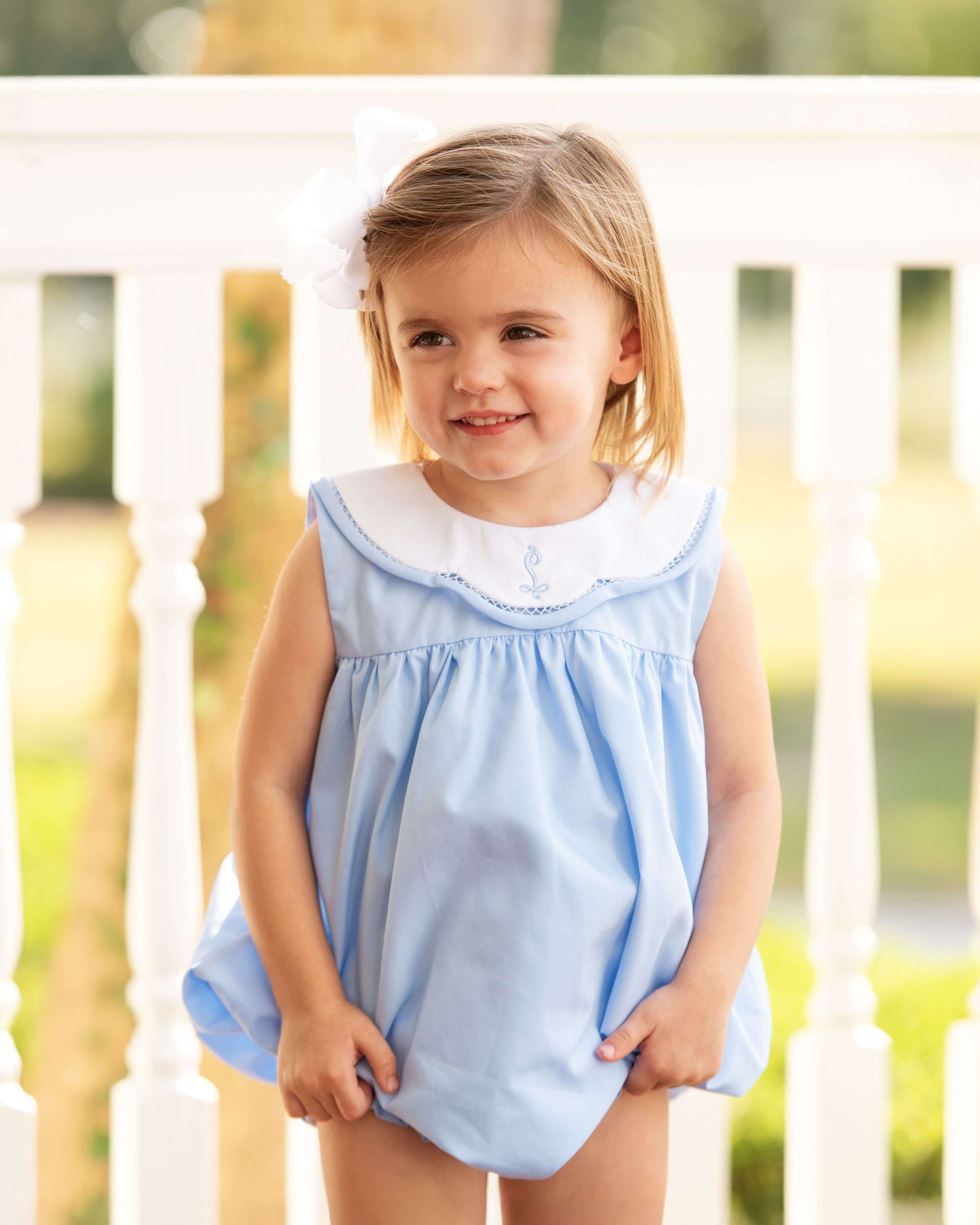 Young girl wearing a light blue dress with white collar, standing on a wooden deck.