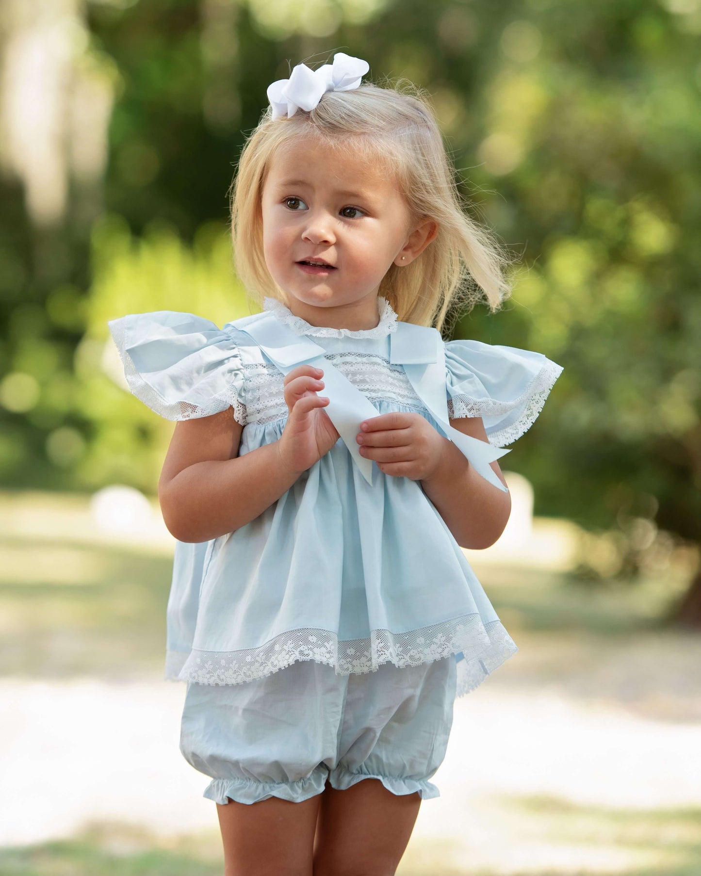 Young girl wearing a light blue dress with white lace details outdoors.