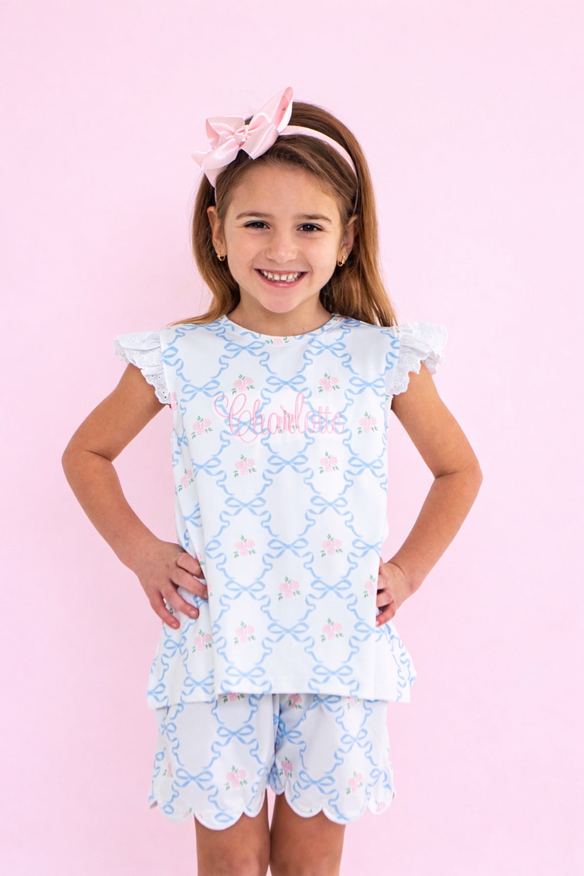 Young girl wearing a light blue play set with floral patterns on a pink background