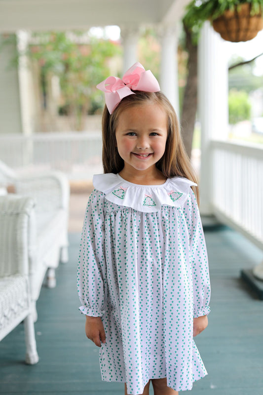 Young girl wearing a patterned dress with a large pink bow on a porch