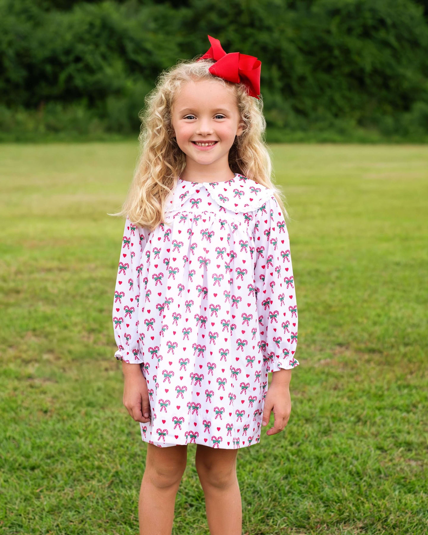 Young girl wearing a patterned dress with a red bow in a grassy field