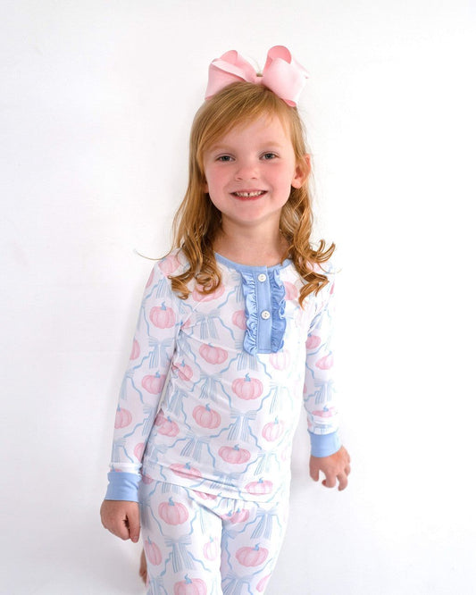 Young girl wearing a patterned pajama set with a pink bow in her hair on a white background