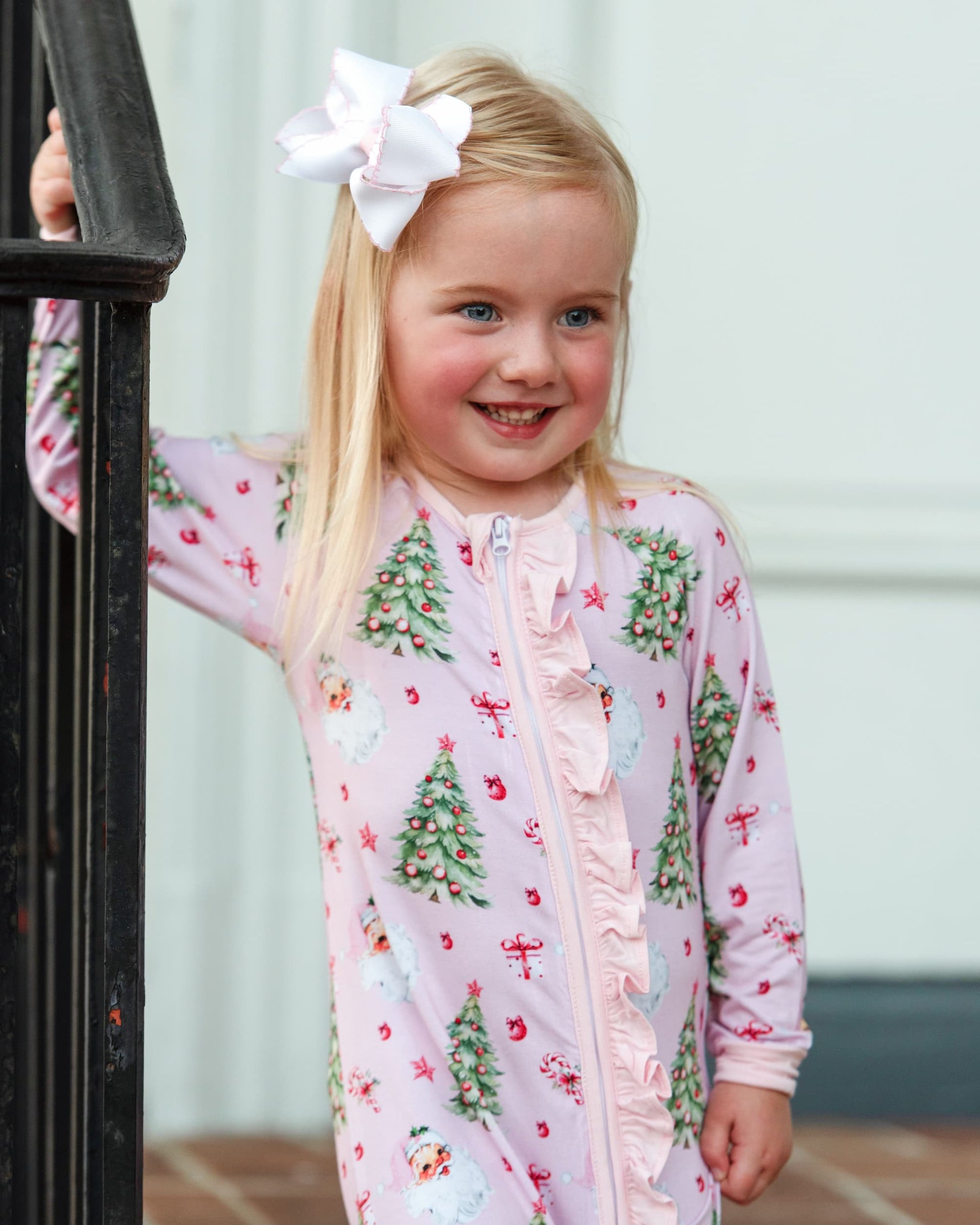 Young girl wearing a pink Christmas-themed outfit with a large white bow in her hair.