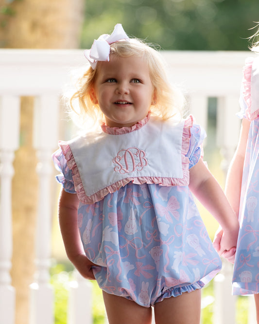 Young girl wearing a pink and blue dress with a bib outdoors.