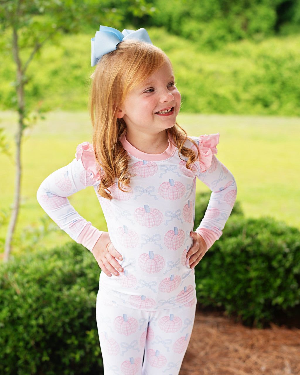 Young girl wearing a pink and blue  pajama set with ruffled sleeves outdoors.