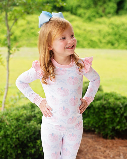 Young girl wearing a pink and blue pajama set with ruffled sleeves outdoors.