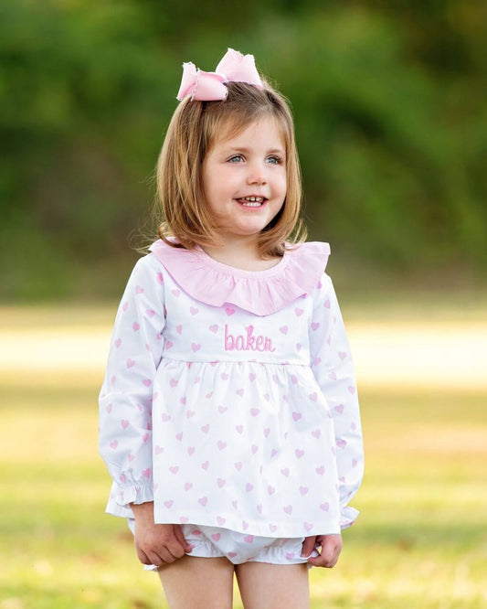 Young girl wearing a pink and white outfit with a bow in her hair, standing outdoors.