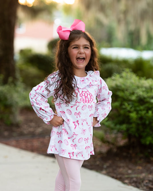 Young girl wearing a pink and white patterned top with a large pink bow outdoors.