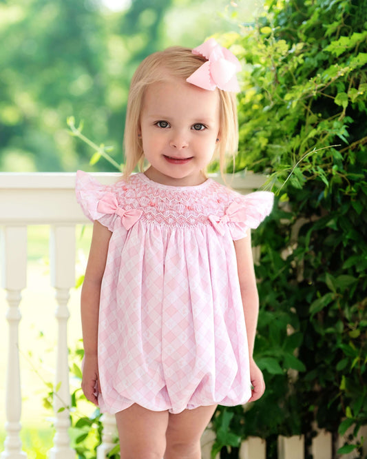 Young girl wearing a pink bubble with a bow in her hair, standing outdoors.