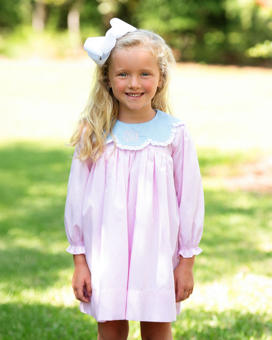 Young girl wearing a pink dress with a blue collar outdoors on a sunny day.
