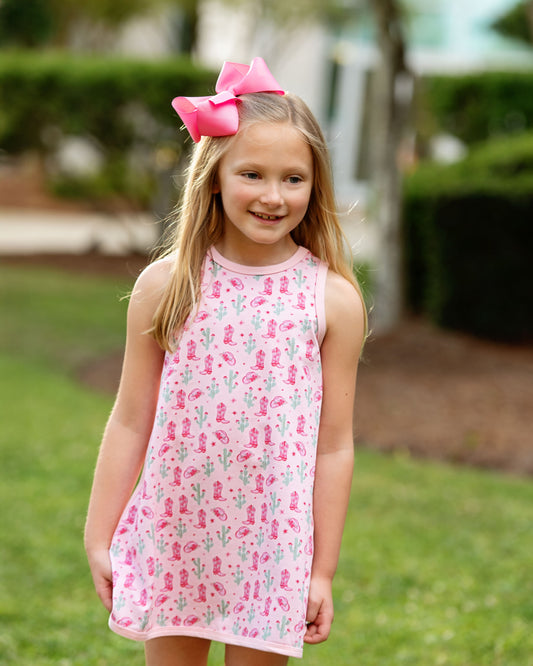 Young girl wearing a pink dress with a floral pattern and a large pink bow outdoors.