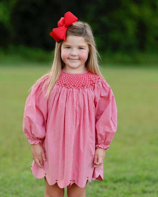 Young girl wearing a pink dress with a red bow in her hair, standing outdoors on grass.