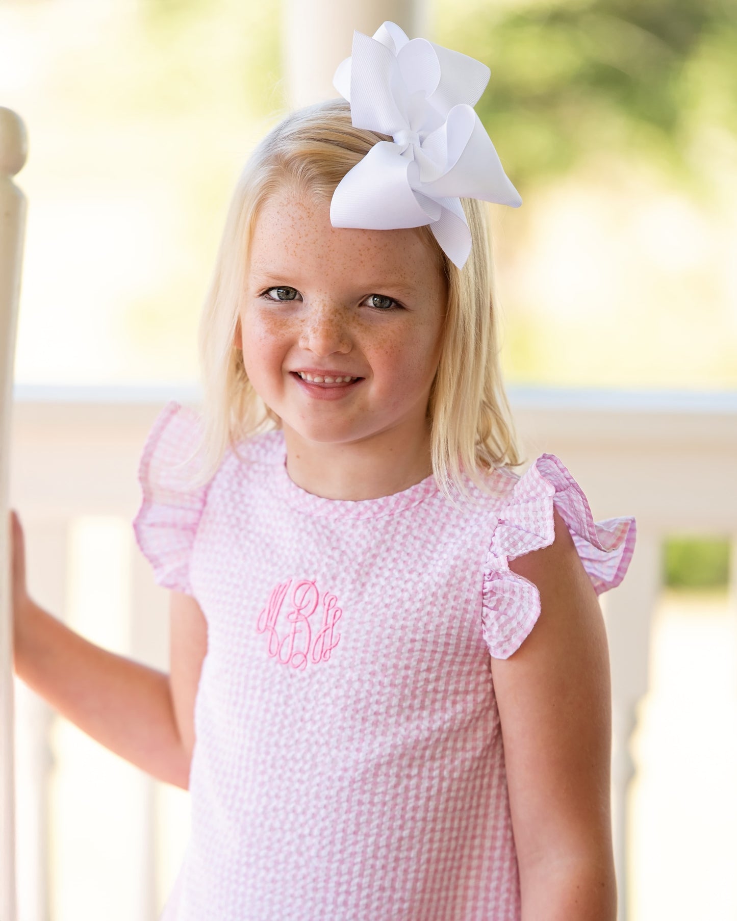 Young girl wearing a pink dress with a white bow in her hair, standing outdoors.