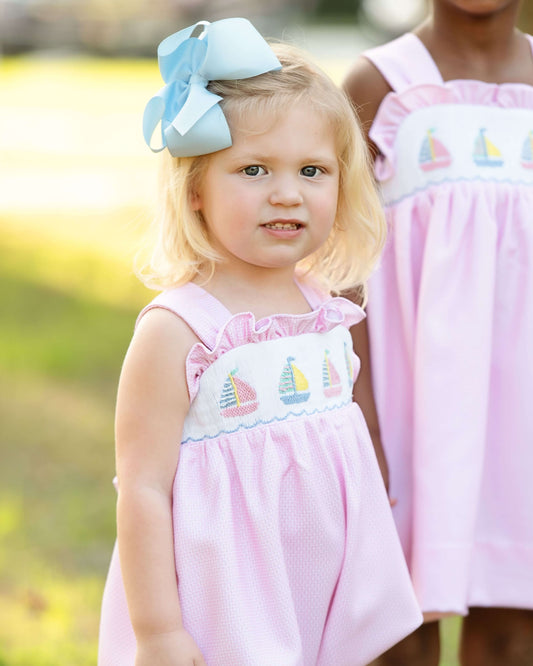 Young girl wearing a pink dress with sailboat embroidery outdoors.