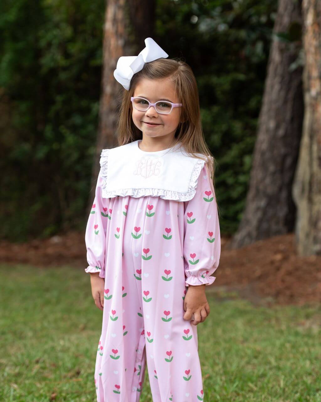 Young girl wearing a pink floral outfit with a white collar, standing outdoors.