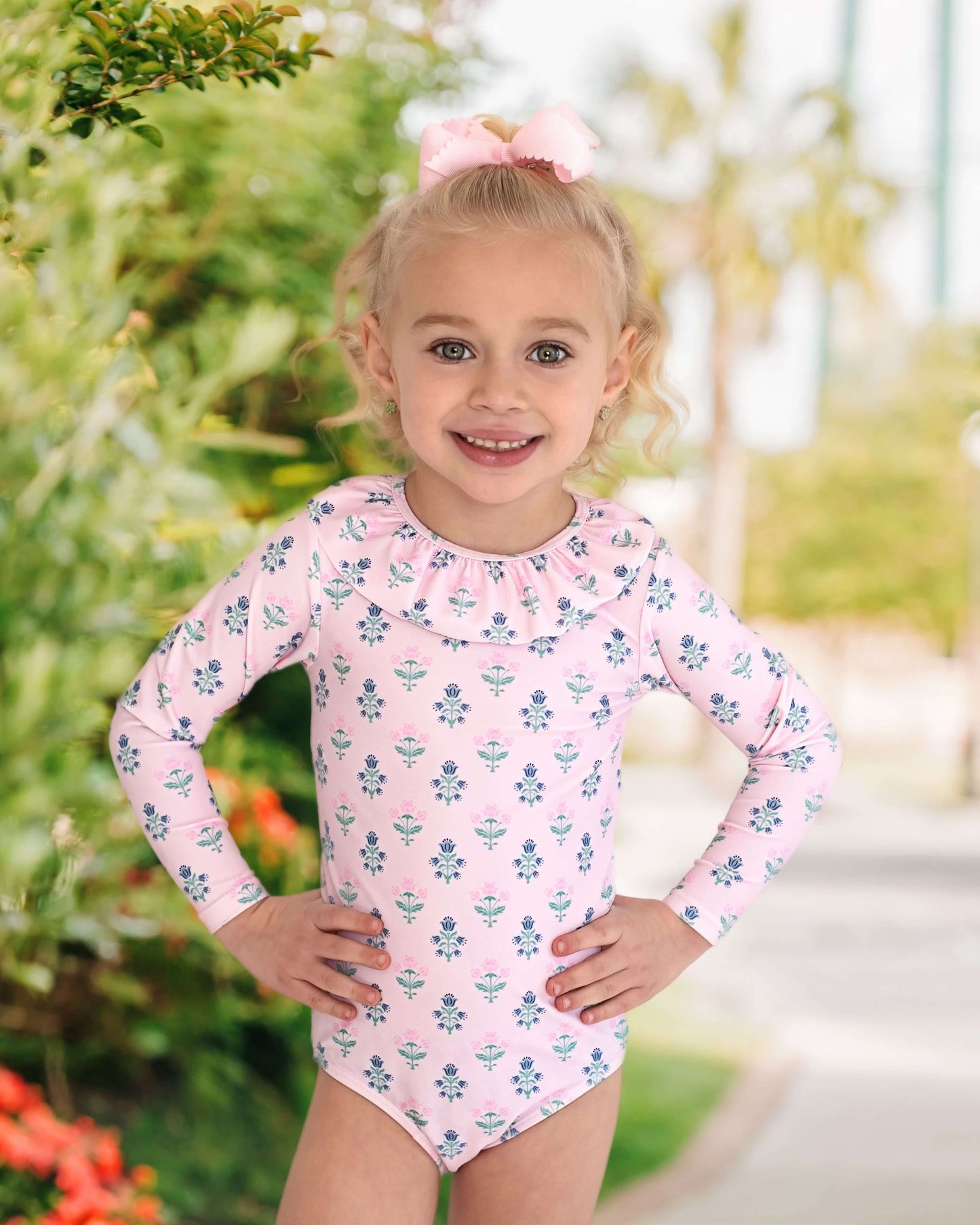 Young girl wearing a pink floral swimsuit with long sleeves outdoors.