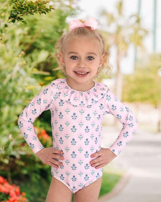Young girl wearing a pink floral swimsuit with long sleeves outdoors.