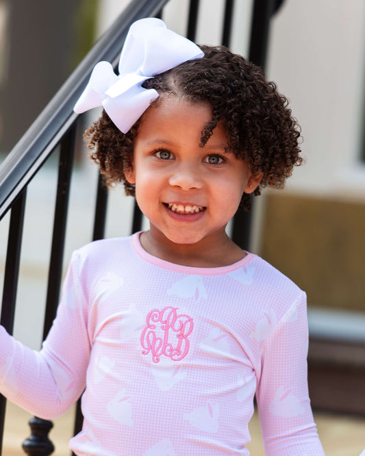 Young girl wearing a pink long-sleeve shirt with a bow in her hair, standing outdoors.