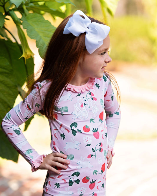 Young girl wearing a pink long-sleeve shirt with a strawberry pattern, standing outdoors.