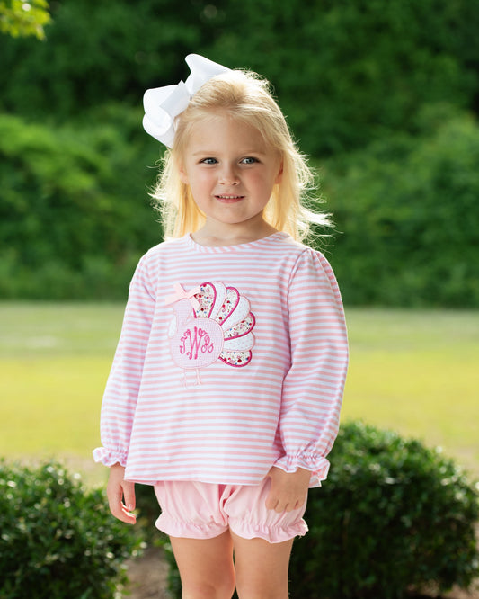 Young girl wearing a pink outfit with a turkey applique in the center