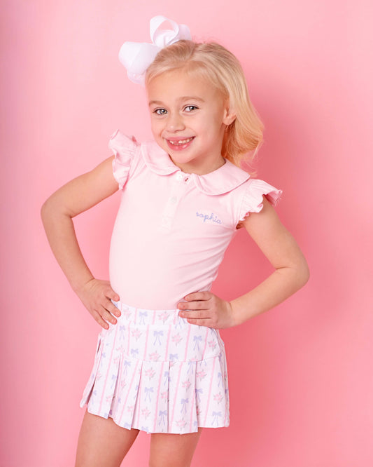 Young girl wearing a pink outfit with a white bow on a pink background