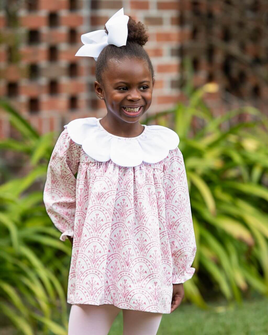 Young girl wearing a pink patterned legging set with a white collar outdoors.