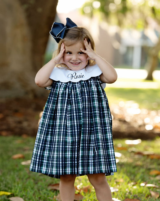 Young girl wearing a plaid dress with a large bow outdoors