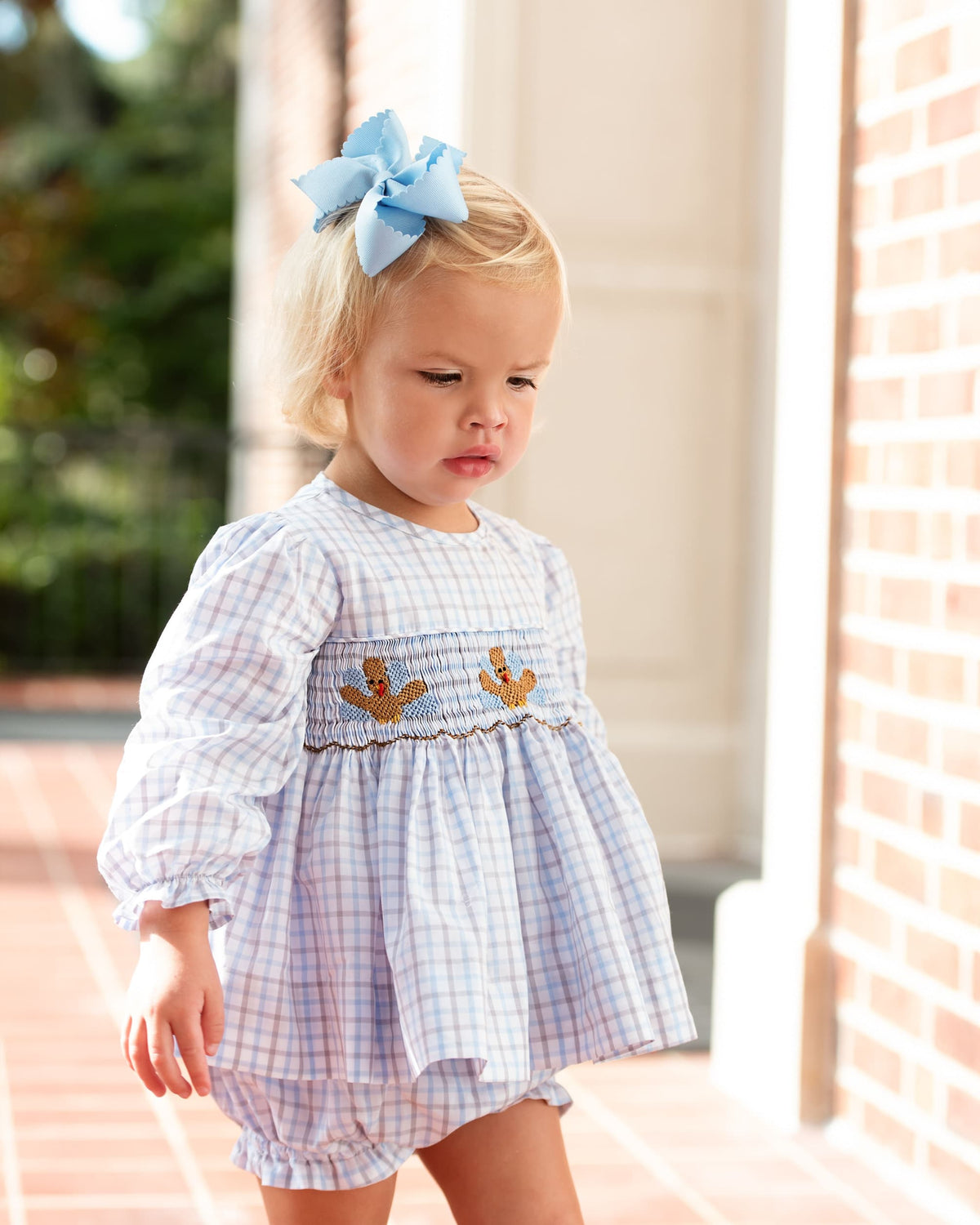 Young girl wearing a plaid outfit with smocked turkeys on it and a blue bow on her hair