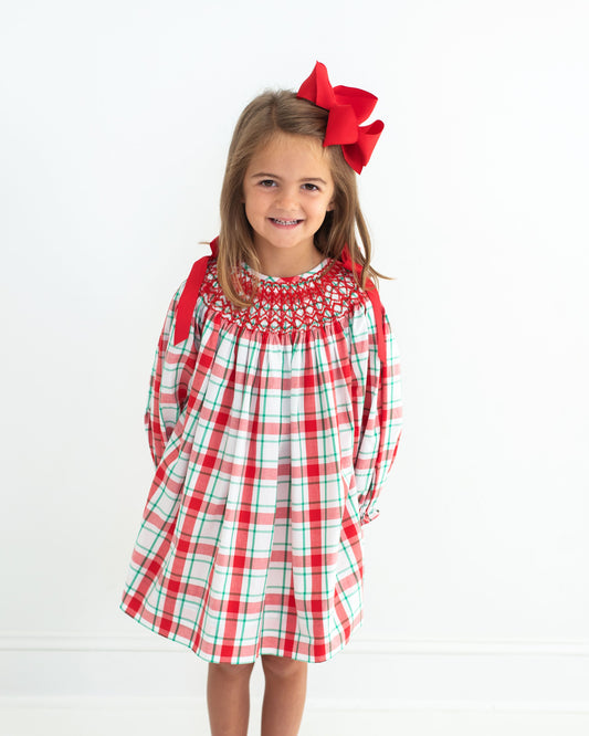 Young girl wearing a red and green plaid dress with a large red bow on a white background