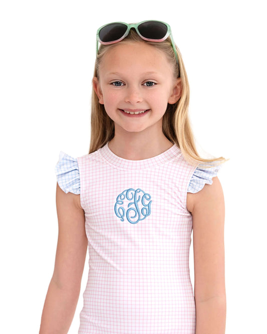 Young girl wearing a white checkered dress with ruffled sleeves and sunglasses on her head against a white background