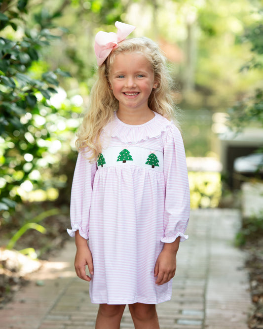 Young girl wearing a white dress with green tree designs outdoors.