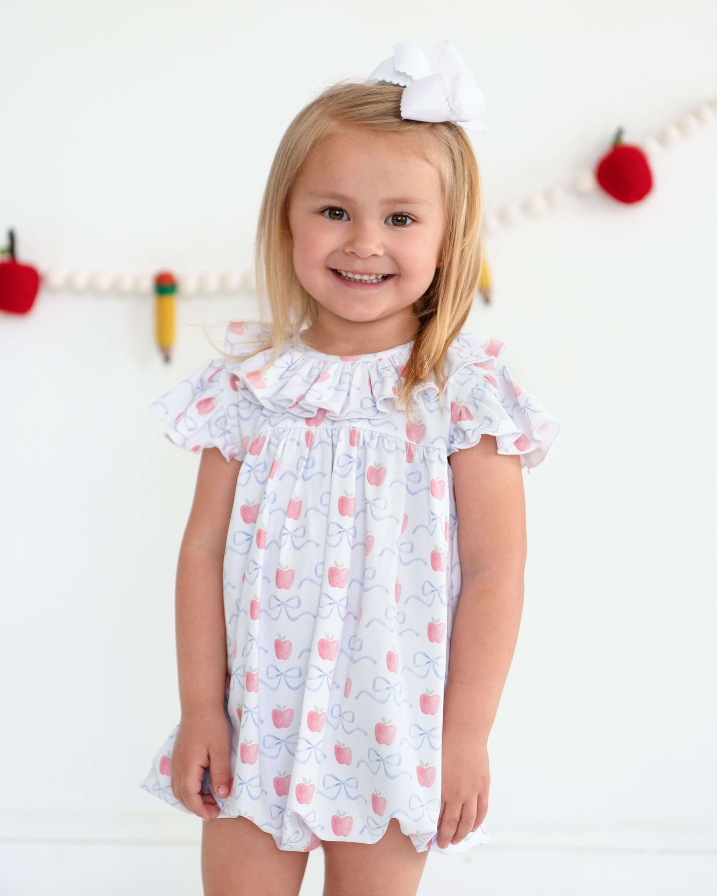 Young girl wearing a white dress with pink cherry pattern against a white background