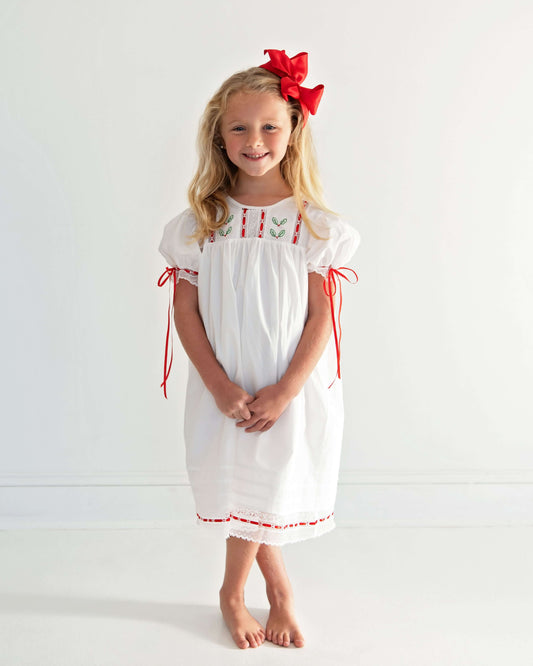 Young girl wearing a white dress with red accents and a red bow in her hair against a white background