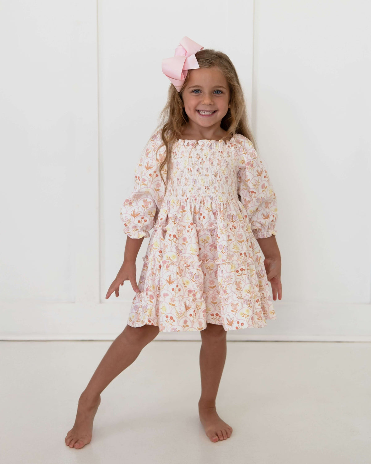 Young girl wearing floral dress and a pink bow standing in a white studio