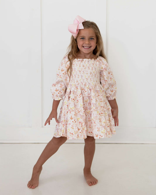 Young girl wearing floral dress and a pink bow standing in a white studio